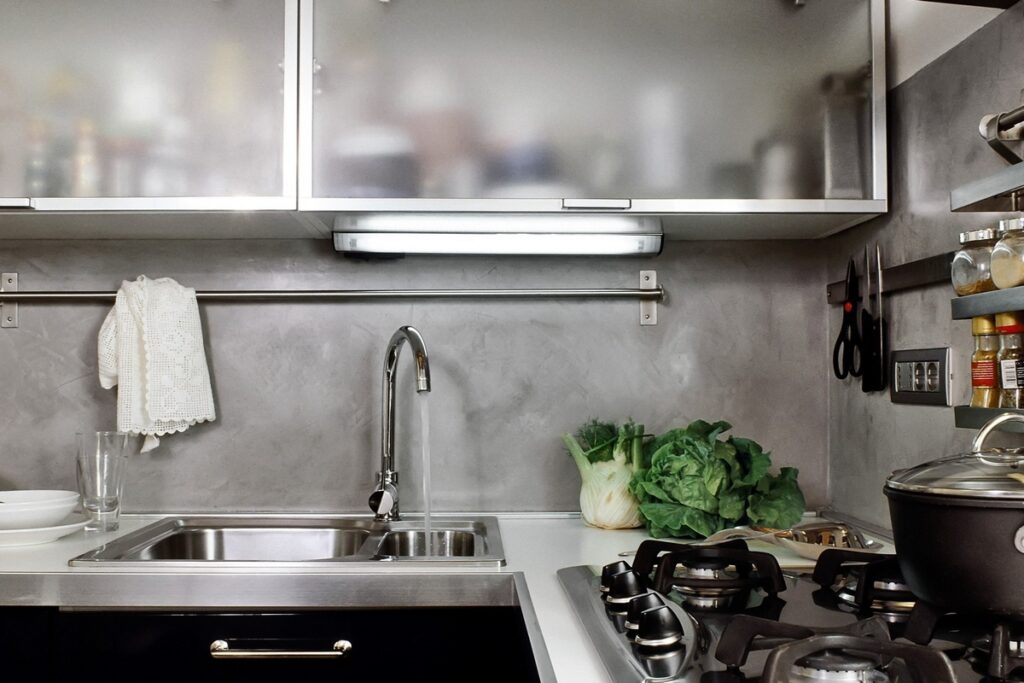 Kuchnia z mikrocementu z widocznym fartuchiem ściennym o delikatnej strukturze i stonowanym kolorze. Mikrocement w kuchni zastępuje tradycyjne płytki między szafkami.