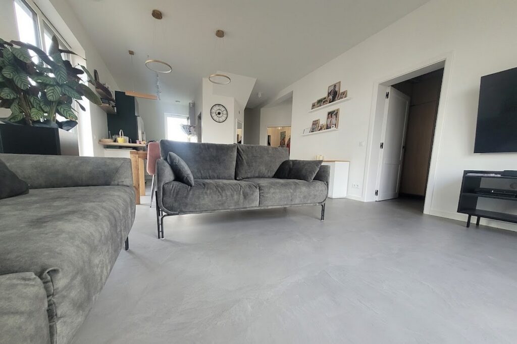 Szara podłoga z mikrocementu w salonie, widoczna na dużej, jednolitej powierzchni. Mikrocement na podłodze wygląda jak beton i pasuje do loftowych aranżacji.