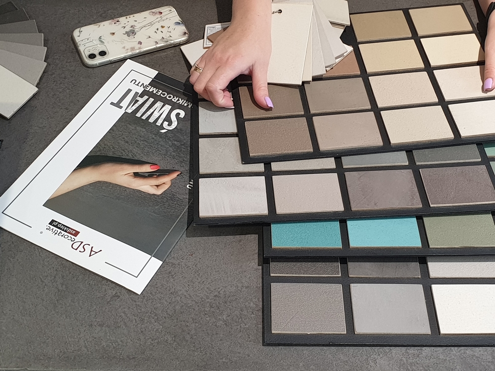 Zestaw pr&oacute;bek mikrocementu o r&oacute;żnych odcieniach i strukturach przygotowany do por&oacute;wnania kolor&oacute;w. Pr&oacute;bki pomagają ocenić kolory mikrocementu w naturalnym oświetleniu wnętrza.