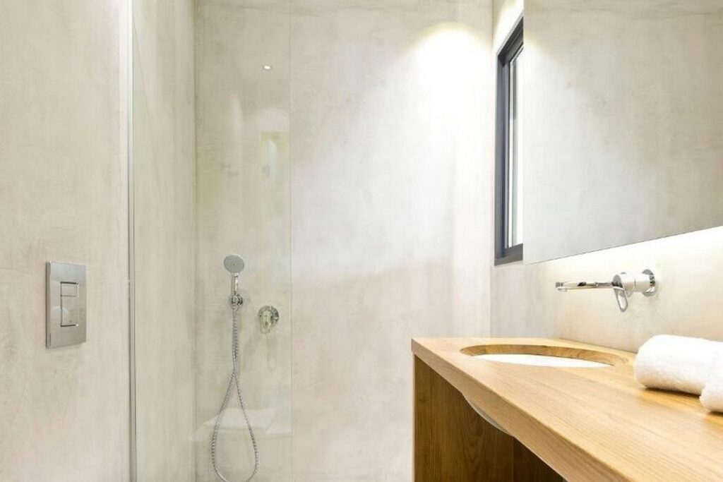 Jasna łazienka z mikrocementem na ścianach i podłodze oraz minimalistyczną zabudową. Zabezpieczenie mikrocementu lakierem poliuretanowym zapewnia szczelność powierzchni w strefach mokrych.