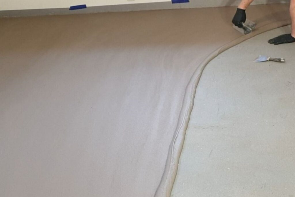 Aplikacja pierwszej warstwy podkładowej BASE na przygotowanej powierzchni posadzki. To etap budujący bazę pod p&oacute;źniejsze warstwy, kt&oacute;re tworzą podłogę z mikrocementu.