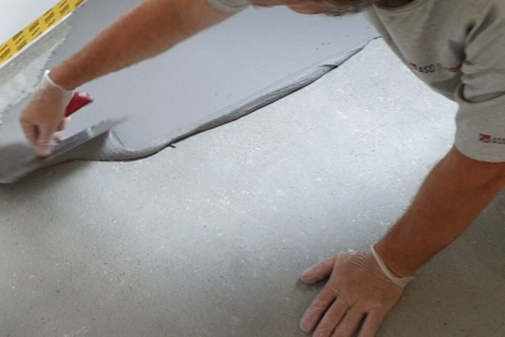 Aplikacja warstwy BASE jako podkładu pod mikrocement pokazuje budowanie grubości i wzmocnienie podłoża, co jest ważne szczeg&oacute;lnie na podłogach przed wykonaniem warstw dekoracyjnych.