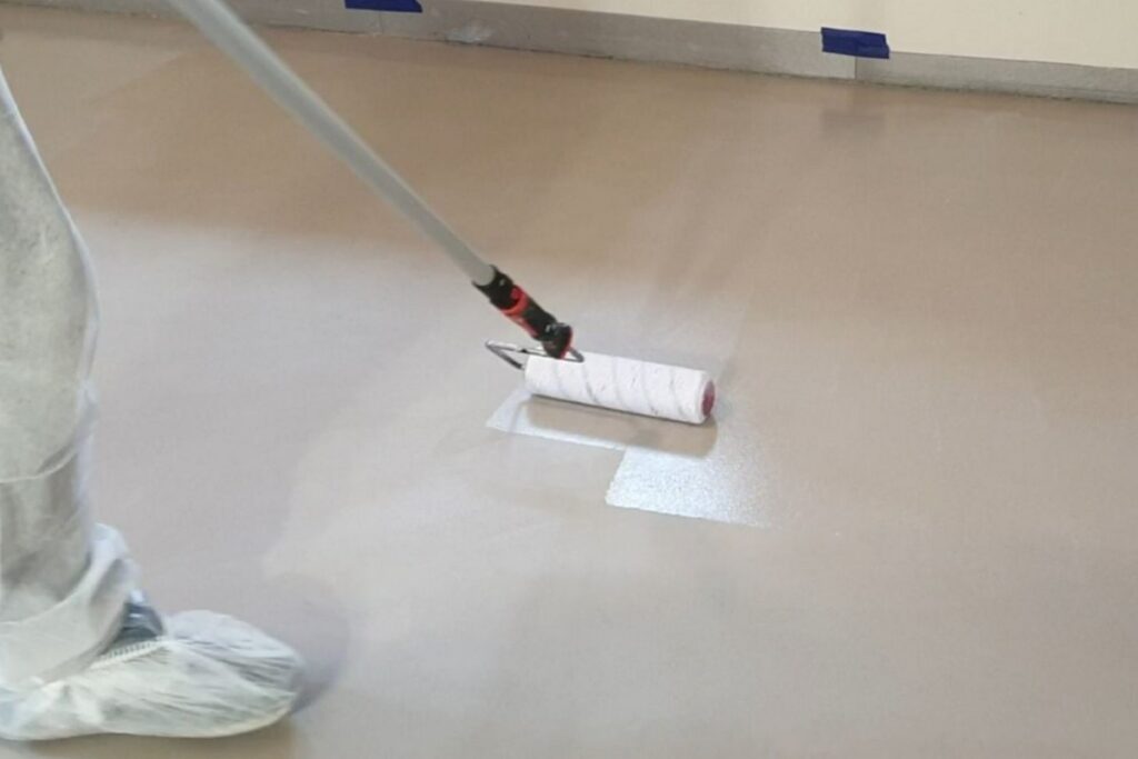 Lakierowanie podłogi z mikrocementu pokazuje końcowy etap zabezpieczenia, kt&oacute;ry zwiększa odporność na ścieranie i ułatwia codzienne czyszczenie w intensywnie użytkowanych pomieszczeniach.