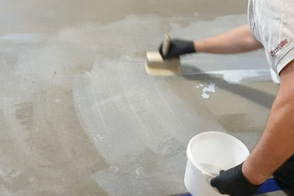 Gruntowanie podłoża pod mikrocement pokazuje aplikację gruntu PRIMER C, kt&oacute;ra poprawia przyczepność i stabilizuje powierzchnię przed nakładaniem kolejnych warstw systemu.