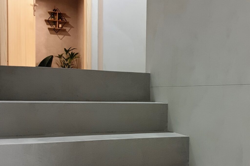 Schody z mikrocementu w strukturze bardziej wyrazistej, z widoczną fakturą i niuansami kolorystycznymi. Taki mikrocement na schodach sprzyja lepszym właściwościom antypoślizgowym i maskuje drobne ślady użytkowania.