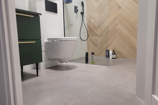 Nowoczesna łazienka z bezspoinową powierzchnią ścian i podłogi wykonaną z mikrocementu. Funkcjonalne zastosowanie mikrocementu zapewnia łatwe utrzymanie czystości i sp&oacute;jny wygląd wnętrza.