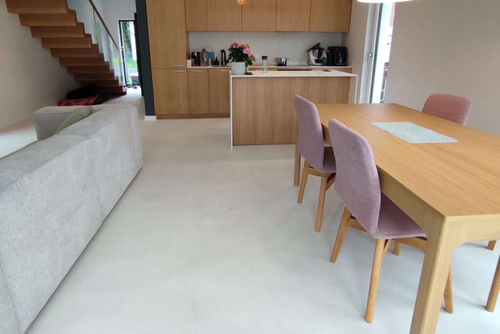 Nowoczesna kuchnia z jadalnią i jednolitą podłogą z mikrocementu w jasnym kolorze. Mikrocement MEDIUM FAST tworzy ciągłą powierzchnię podłogi bez fug pomiędzy salonem i kuchnią.