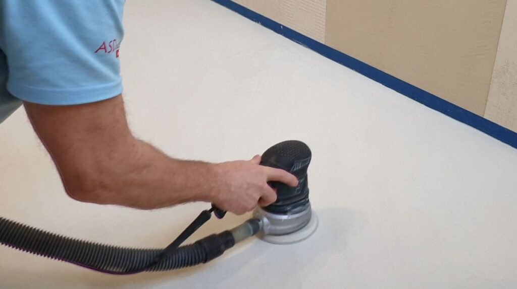 Szlifowanie powierzchni mikrocementu przy użyciu narzędzia szlifierskiego podczas prac wykończeniowych. Proces szlifowania pozwala uzyskać odpowiednią strukturę i przygotować powierzchnię do dalszego zabezpieczenia.