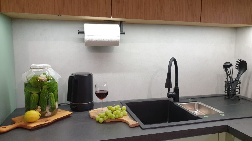 Ściana w kuchni wykończona mikrocementem w neutralnym kolorze, tworząca jednolitą powierzchnię nad blatem. Praktyczne zastosowanie mikrocementu łączy estetykę z odpornością na zabrudzenia.